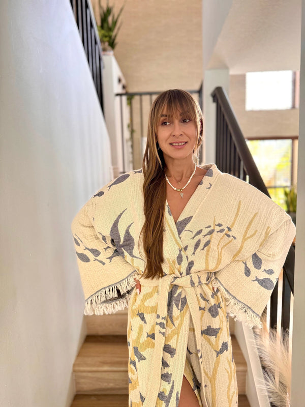 Woman wearing a yellow floral kimono-style garment indoors.